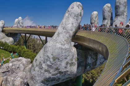The iconic Golden Bridge with giant hand sculptures at Ba Na Hills, Vietnam, under a clear blue sky.