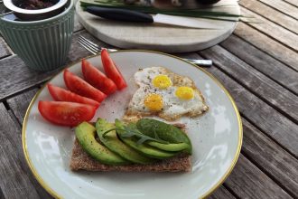 A vibrant outdoor breakfast setup with avocado toast, quail eggs, tomatoes, and tea.