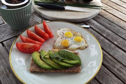 A vibrant outdoor breakfast setup with avocado toast, quail eggs, tomatoes, and tea.